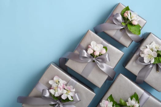 Gray gift boxes with apple flowers and silver ribbons on light blue background. Horizontal, space for your text.