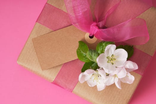 Brown craft gift box with empty tag, apple flowers on pink background. Place for your text