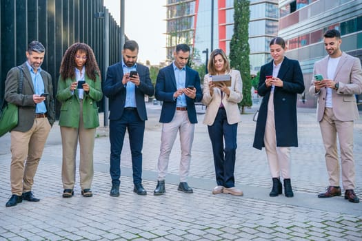 A diverse group of business professionals standing together outdoors, using smartphones. The image represents modern technology, teamwork, and communication, perfect for business, tech, and social concepts.
