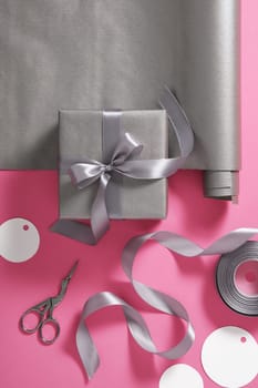 Card with gift wrapping. Gray paper, silver ribbon, scissors on pink background. Vertical, place for text
