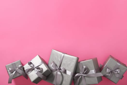 Monochrome gray gift boxes with silver ribbons on pink background. Copyspace