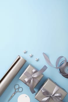 Card with gift wrapping. Gray paper, silver ribbon, scissors on light blue background. Vertical, copyspace