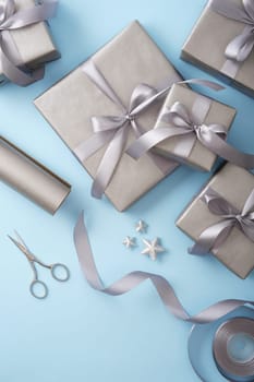 Gift wrapping. Gray paper, silver ribbon, scissors on light blue background. Vertical, place for text