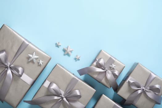 Set of monochrome gray gift boxes with gray ribbons and silver stars on light blue background. Copyspace