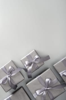 Silver gift boxes with gray ribbons on light background. Vertical, space for your text.