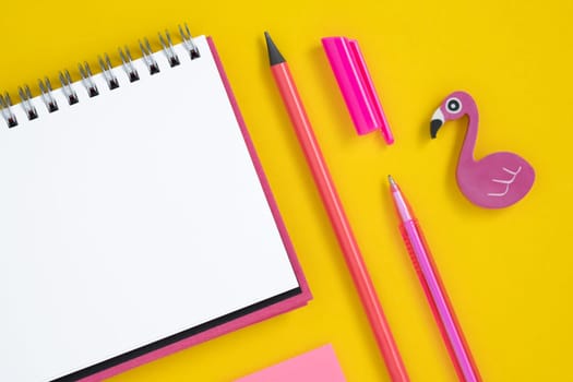 Empty notebook page for your text with pink school and office stationery on yellow background. Eraser in form of flamingo. Flatly.