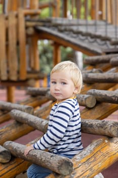 Little boy sitting between wood logs on playground. Vertical shot