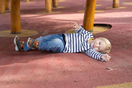 A little funny boy lying on the ground on the playground. Mid shot
