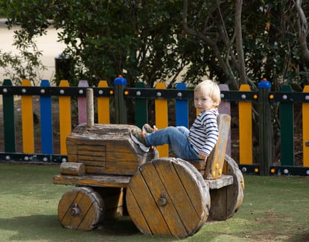 Little boy sitting in a wooden toy tractor on the playground. Mid shot