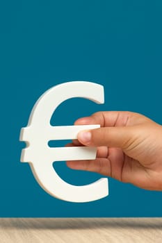White Euro symbol in a hand on a blue background close-up with copy space. Euro exchange rate, economy in Europe or inflation. High quality photo