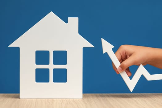 Raising mortgage interest rates. Increasing the bank's margin when buying real estate. A white house symbol with a graph arrow pointing up, on a blue background, close-up. Copy space