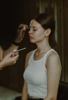 Portrait of a young beautiful Caucasian girl sitting on a chair in a beauty salon and doing her makeup, side view.