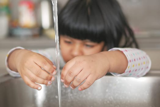 child washing hands at kitchen sink .