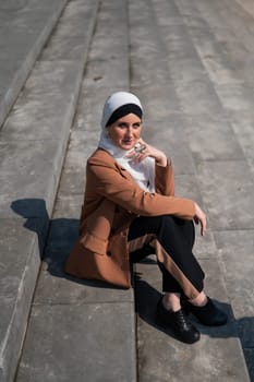 A young woman dressed in a hijab and a business suit is sitting on the stairs