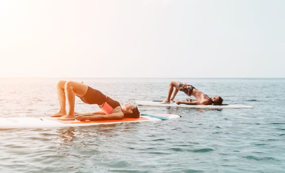 Woman man sup yoga. Happy young sporty couple practising yoga pilates on paddle sup surfboard. Female stretching doing workout on sea water. Modern family outdoor summer sport activity