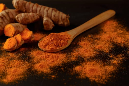 fresh turmeric root and ground turmeric in a wooden spoon isolated on black background and copy space