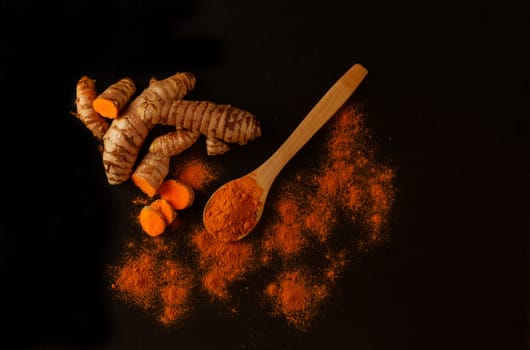 fresh turmeric root and ground turmeric in a wooden spoon isolated on black background and copy space