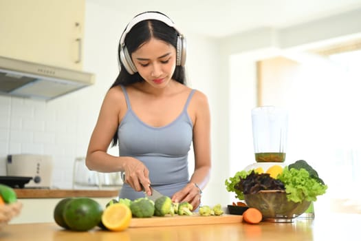 Pretty young woman preparing ingredients for making vegetables smoothie in kitchen. Dieting, healthy lifestyle concept.