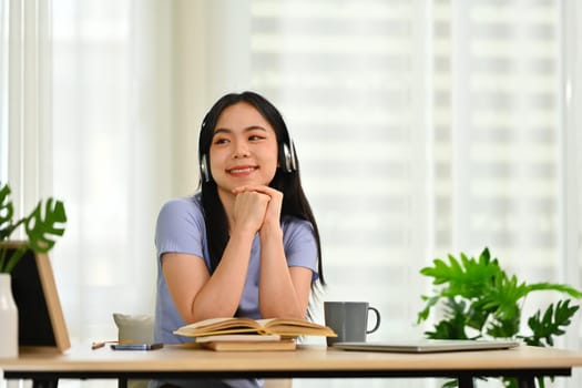 Relaxed young woman enjoying favorite track, listening to music through headphones while sitting in cozy home.