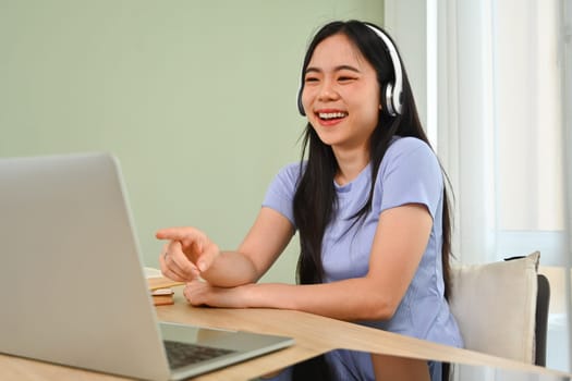 Cheerful asian girl wearing headphones, enjoying watching video on laptop.