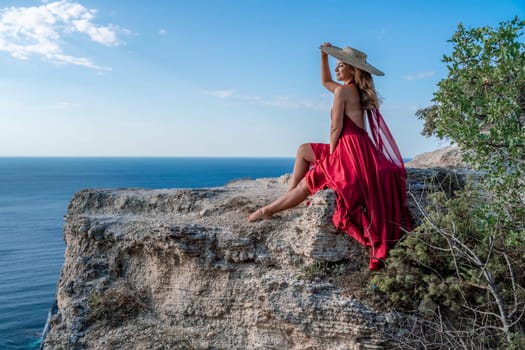 A girl with flowing hair in a long red dress sits on a rock above the sea. The stone can be seen in the sea