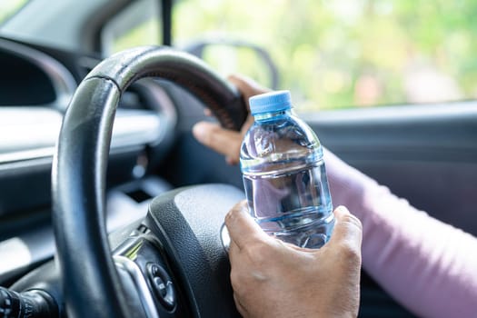 Asian woman driver holding bottle for drink water while driving a car. Plastic hot water bottle cause fire.