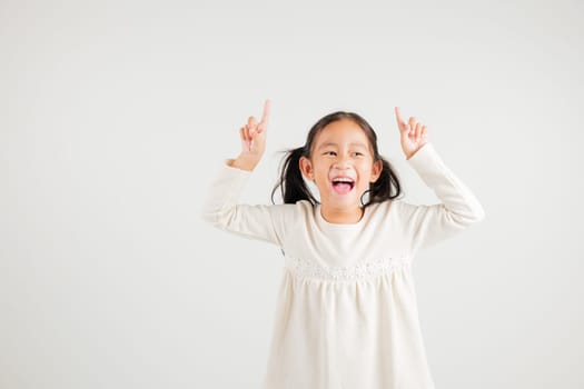 Asian happy portrait cute young kid girl makes gesture fingers point upwards above presenting product something, studio shot isolated on white background, kindergarten children woman smile