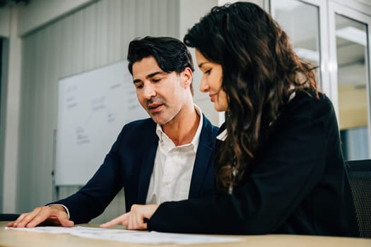 Colleagues in an office setting, working together and planning their business strategy. Teamwork is key as they discuss documents, analyze graphs, and aim for success.