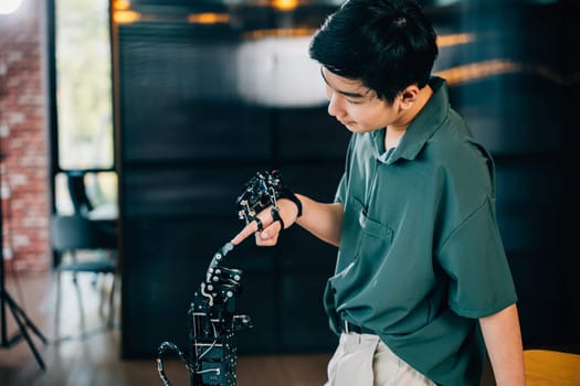 At a technical college a teen boy learns technology by testing a robot hand and arm touching fingers for educational skill enhancement. Embracing AI and futuristic humanity.