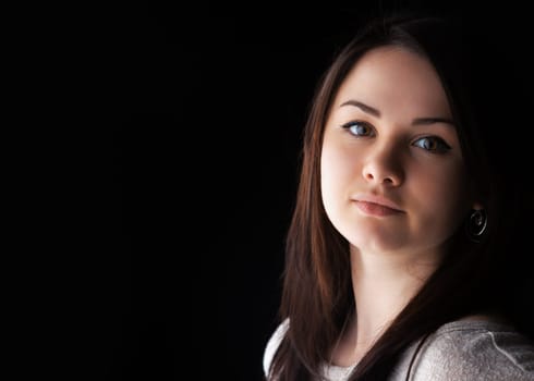 A young woman with long brown hair displays a calm and thoughtful expression. She is positioned in front of a dark background, accentuating her features and soft expression.