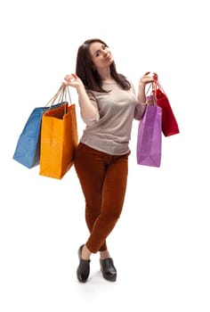 A young woman stands in a bright studio, joyfully holding four colorful shopping bags. She wears a casual outfit and has a playful expression while enjoying her shopping experience.