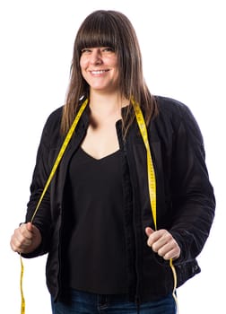 Forty something woman wearing a black motocycle coat, holding a yellow measuring tape around her neck against a white background