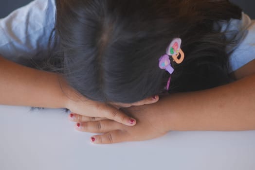A young child peacefully rests her head on her delicate arms, completely lost in deep thought