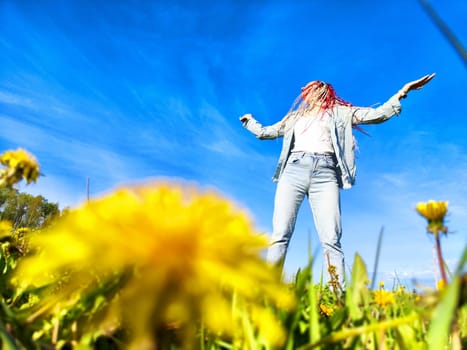 In a sunny field filled with dandelions, an individual joyfully dances, embracing the beauty of nature and the bright blue sky.