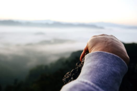 Human hand on the top of the mountain with the sea of fog background.