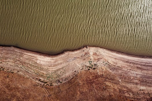drone view of river with rippled water surface flowing near stony shore with dried surface in nature, concept of environment and ecology