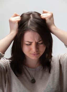 A young woman with brown hair holds her head in her hands, looking stressed and distressed.