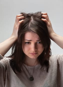 A young woman with brown hair holds her head in her hands, looking down with a troubled expression.