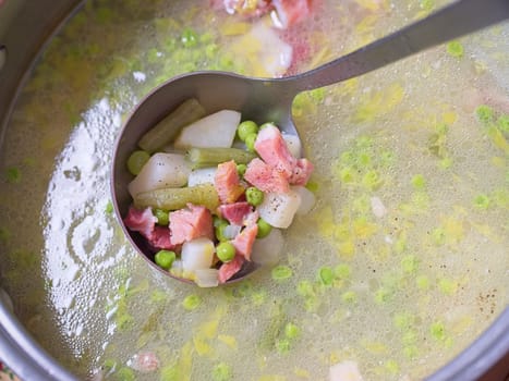 Scooping out a ladle full of ham, potato, and pea soup from the pot.