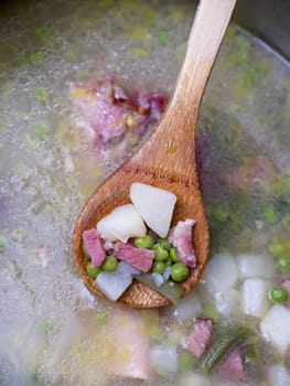 A heaping spoon full of delicious ham and pea soup with potatoes scooped from the pot.