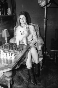 A girl holds a white fluffy dog ​​in her arms, Black and white photo. The girl is dressed in a white suit, she has long hair, she loves her dog, a Spitz. The dog is white and fluffy