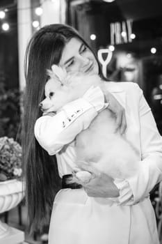 A girl holds a white fluffy dog ​​in her arms, Black and white photo. The girl is dressed in a white suit, she has long hair, she loves her dog, a Spitz. The dog is white and fluffy