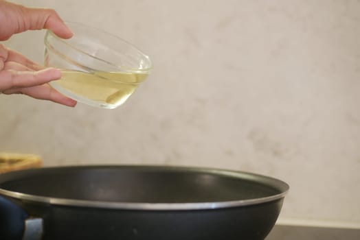 A hand skillfully pours oil into a frying pan, ready for cooking fresh ingredients