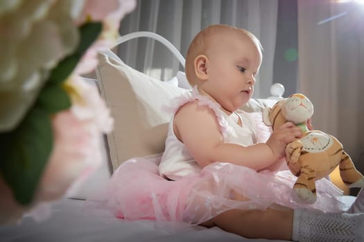 A baby in a pink tutu crawls on a bed surrounded by soft pillows, exploring the cozy space.