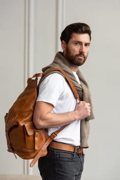 A fashionable man stands with a yellow brown backpack in a contemporary room, embodying urban style and professionalism.