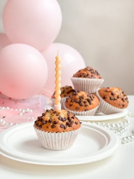 Chocolate chip muffins with birthday candle and pink balloons in background. Birthday concept.