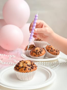 Child celebrating with chocolate chip muffins and pink balloons. Birthday concept.