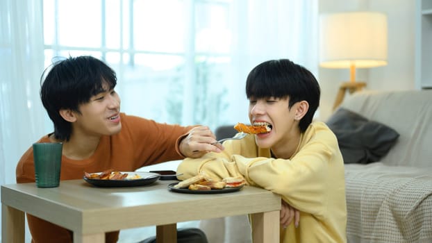 Romantic gay couple enjoys a casual meal together in living room.