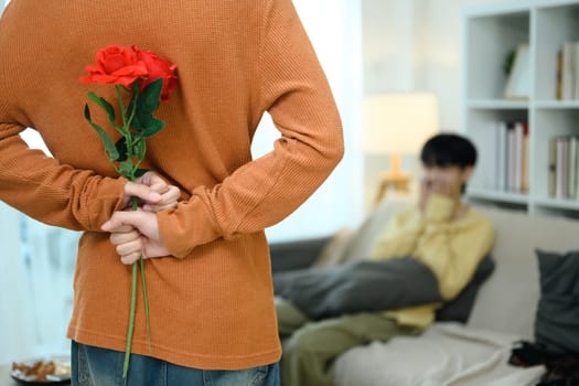 Rear view of man hiding red rose while walking towards his boyfriend preparing to surprise.