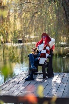 Autumn lake woman dog. She sits by a pond on a wooden pier in autumn and admires nature, holding a Yorkshire terrier in her hands. The concept of tourism, weekends outside the city
